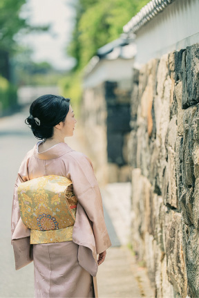 着物姿の女性たちが、生け垣のある道を歩いている。