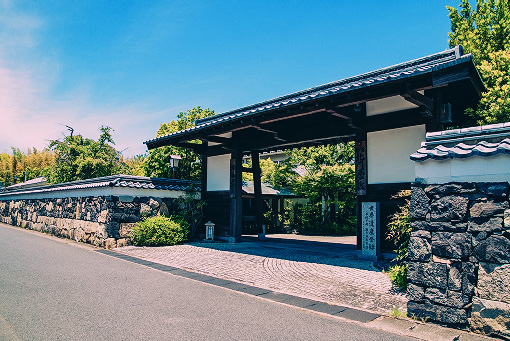青空の下に堂々と構える、石垣と生け垣に囲まれた和風の門構え