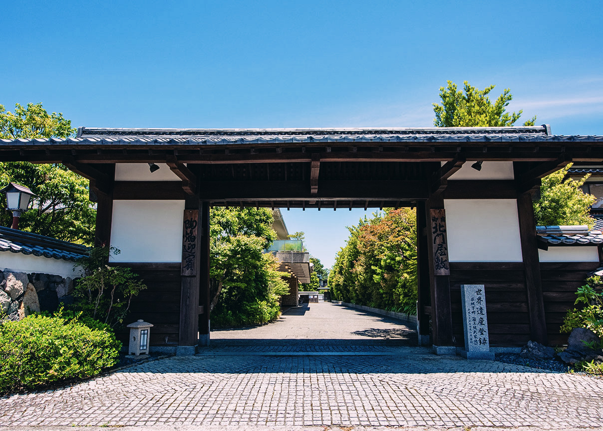 伝統的な門と緑の並木道が迎える、格式ある日本庭園の入口
