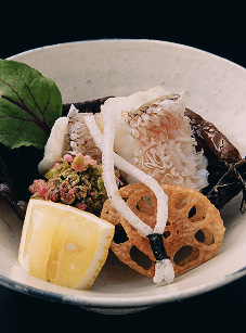 白い器に盛り付けられた白身魚、白い飾り切り、レモン、葉野菜、レンコンの素揚げ、煮物等の和食。