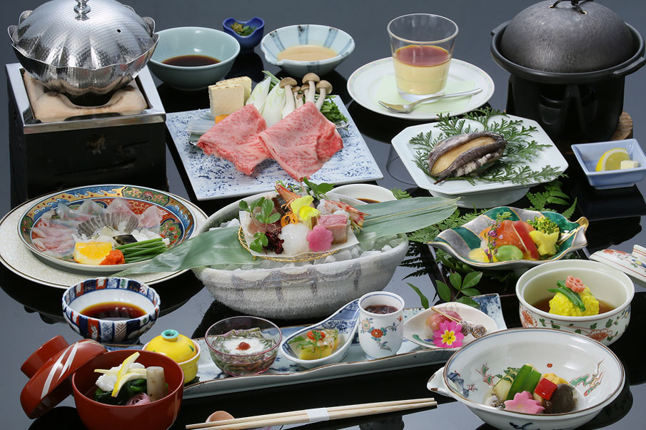 Sumptuous kaiseki dishes are arranged on black tables. A diverse array of dishes are beautifully presented, including beef, sashimi, grilled fish, dressed dishes, nabe dishes, kara-yaki, bowls, and aperitifs.