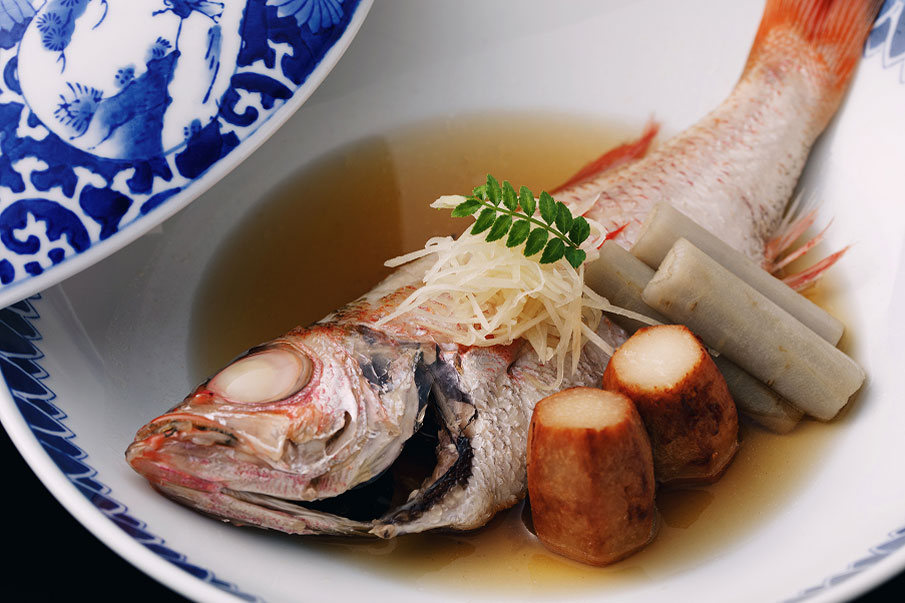 A boiled fish dish served in a Japanese style bowl. Beautifully presented with condiments and vegetables.