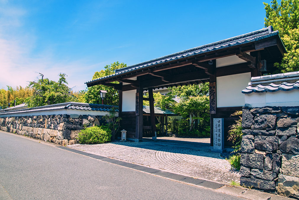 The gate of the north gate house, surrounded by stone walls and hedges, stands majestically under the blue sky.