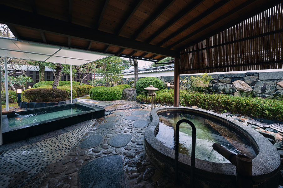 An open-air bath with two stone bathtubs in a lush garden.