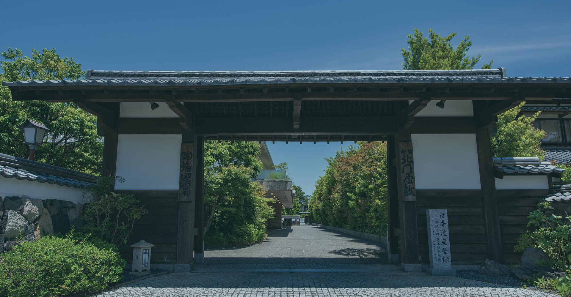 伝統的な門と緑の並木道が迎える、格式ある日本庭園の入口。