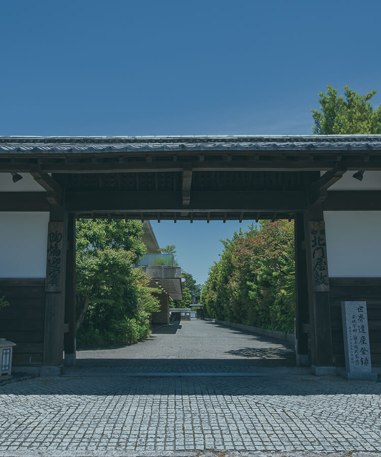 伝統的な門と緑の並木道が迎える、格式ある日本庭園の入口。