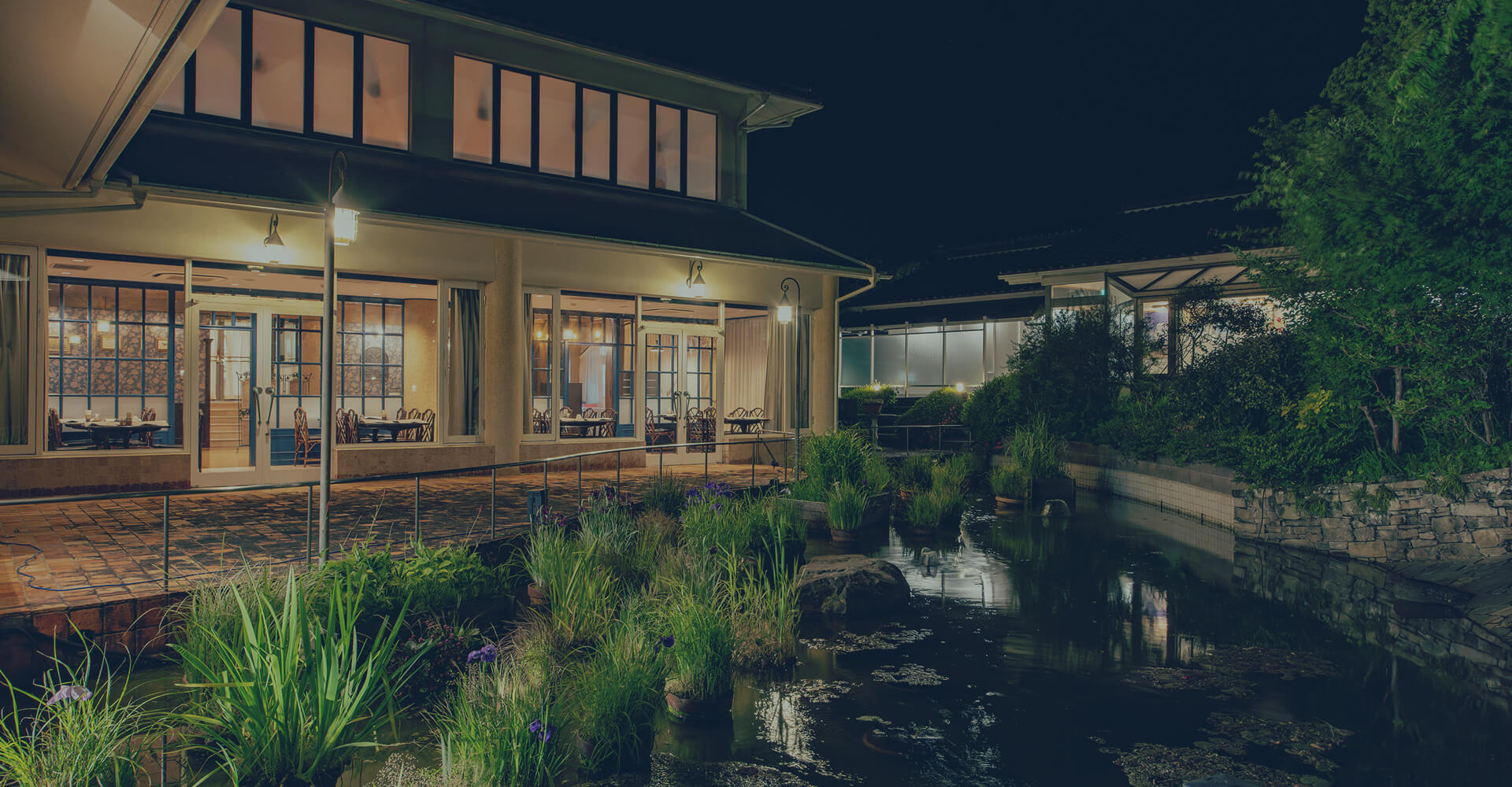 夜の灯りが美しく映る池と、和風旅館の外観が幻想的に照らされた風景。