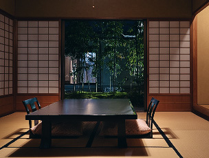夜の和室の様子。畳の上に置かれた黒光りする座卓を挟んで、背もたれのある黒い椅子が二脚置かれています。