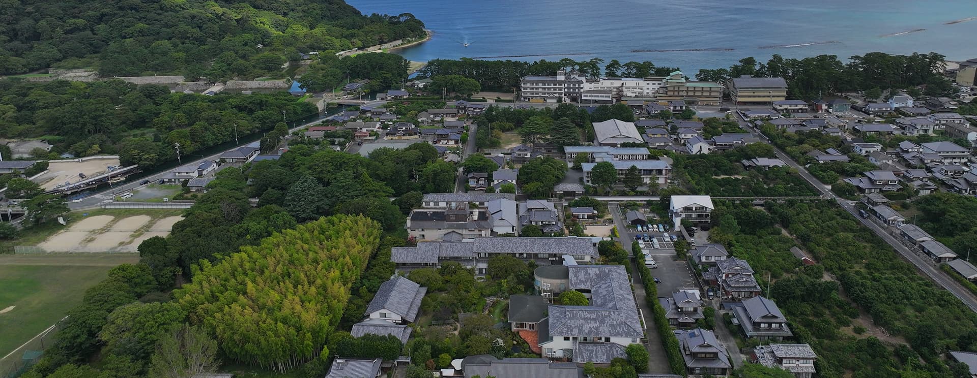 海岸沿いに広がる旅館街の空撮写真。手前には緑豊かなエリアがあり、奥には海と白い建物が見える。